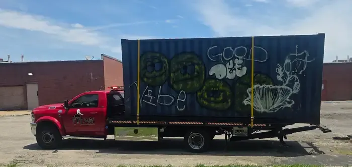 Titan red rollback flatbed hauling a shipping container.