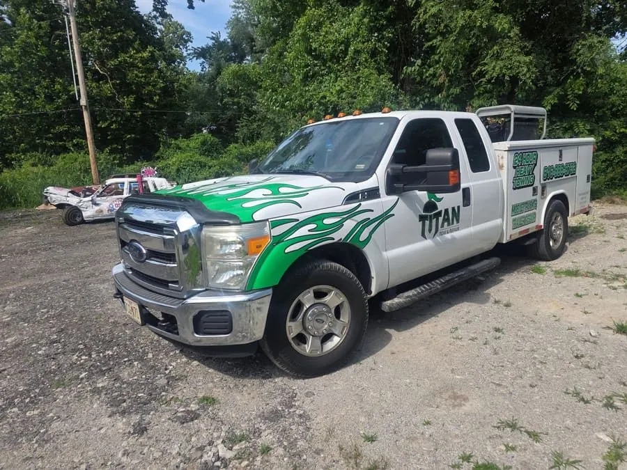 Titan mobile service truck — a white Ford with green flame livery and a service body lettered 24 hour heavy towing and mobile truck and trailer repair.
